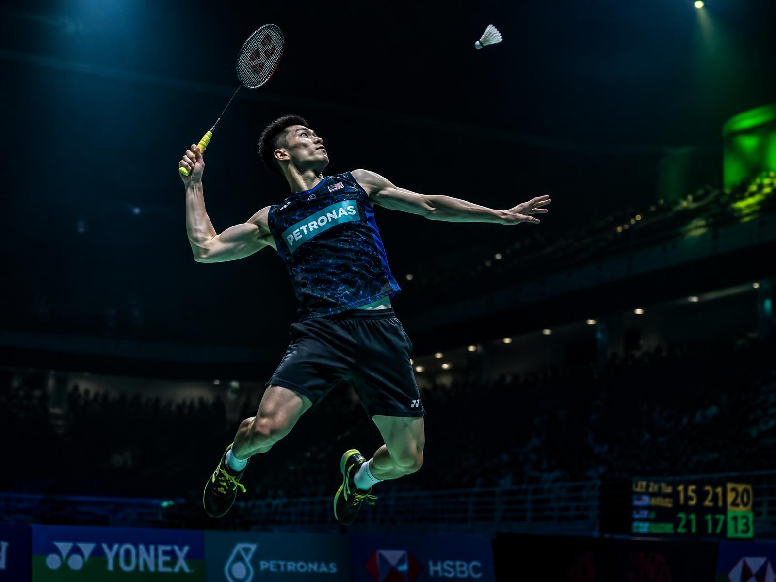 Atleta de badminton em salto para um smash numa arena iluminada